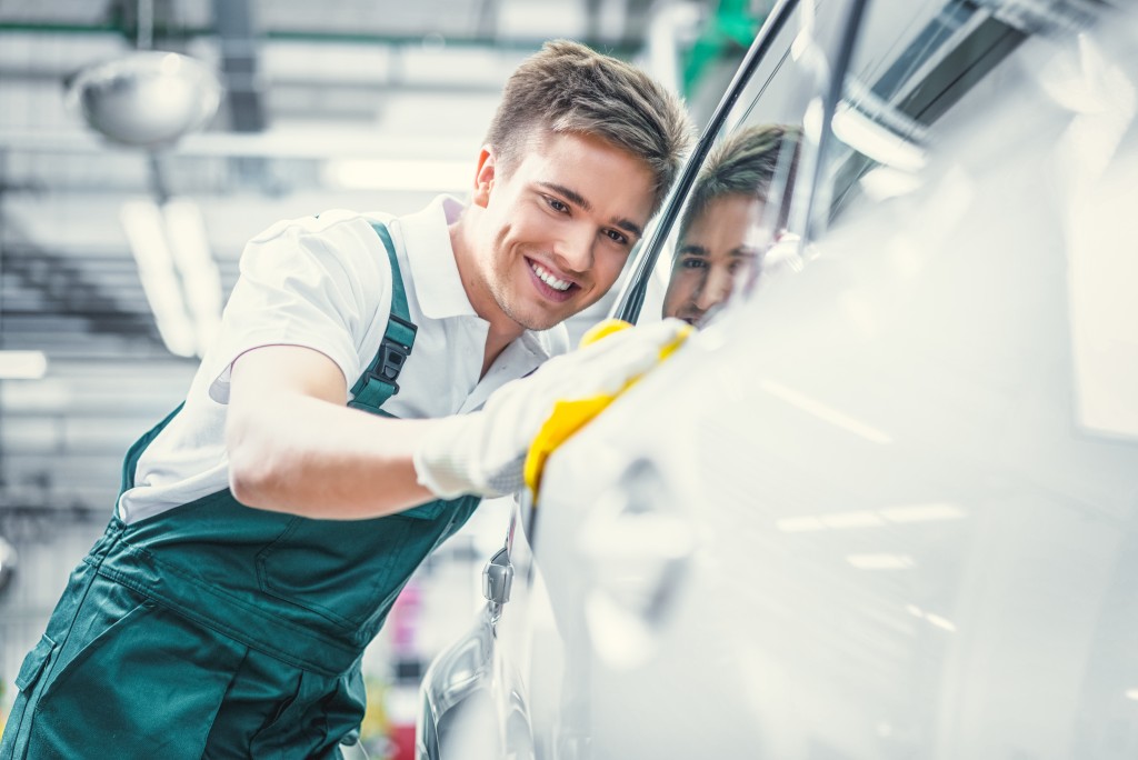 car waash worker smiling while wiping car's surface