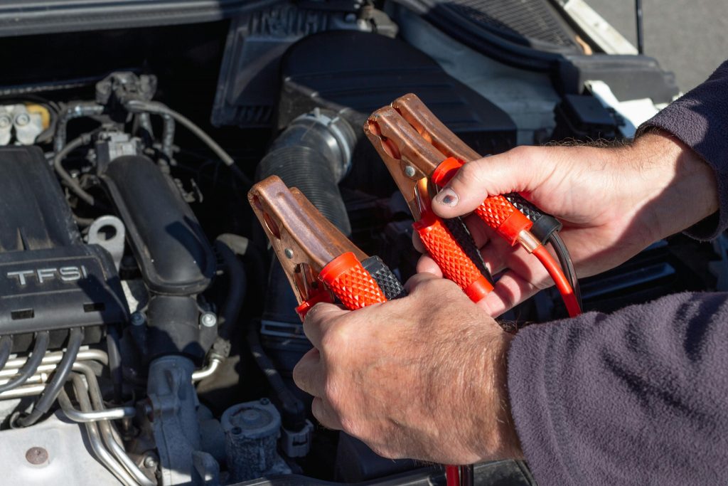 close-up of a man jump starting a car with jumper cables